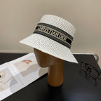White straw hat with a black band featuring 'Christian Dior' on a mannequin head against a neutral background.