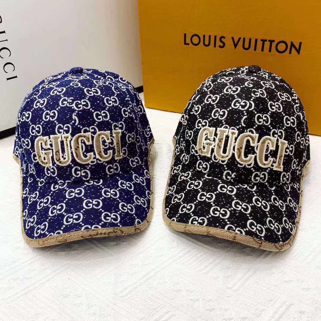 Two Gucci hats with logo patterns on a white surface with a Louis Vuitton box in the background.