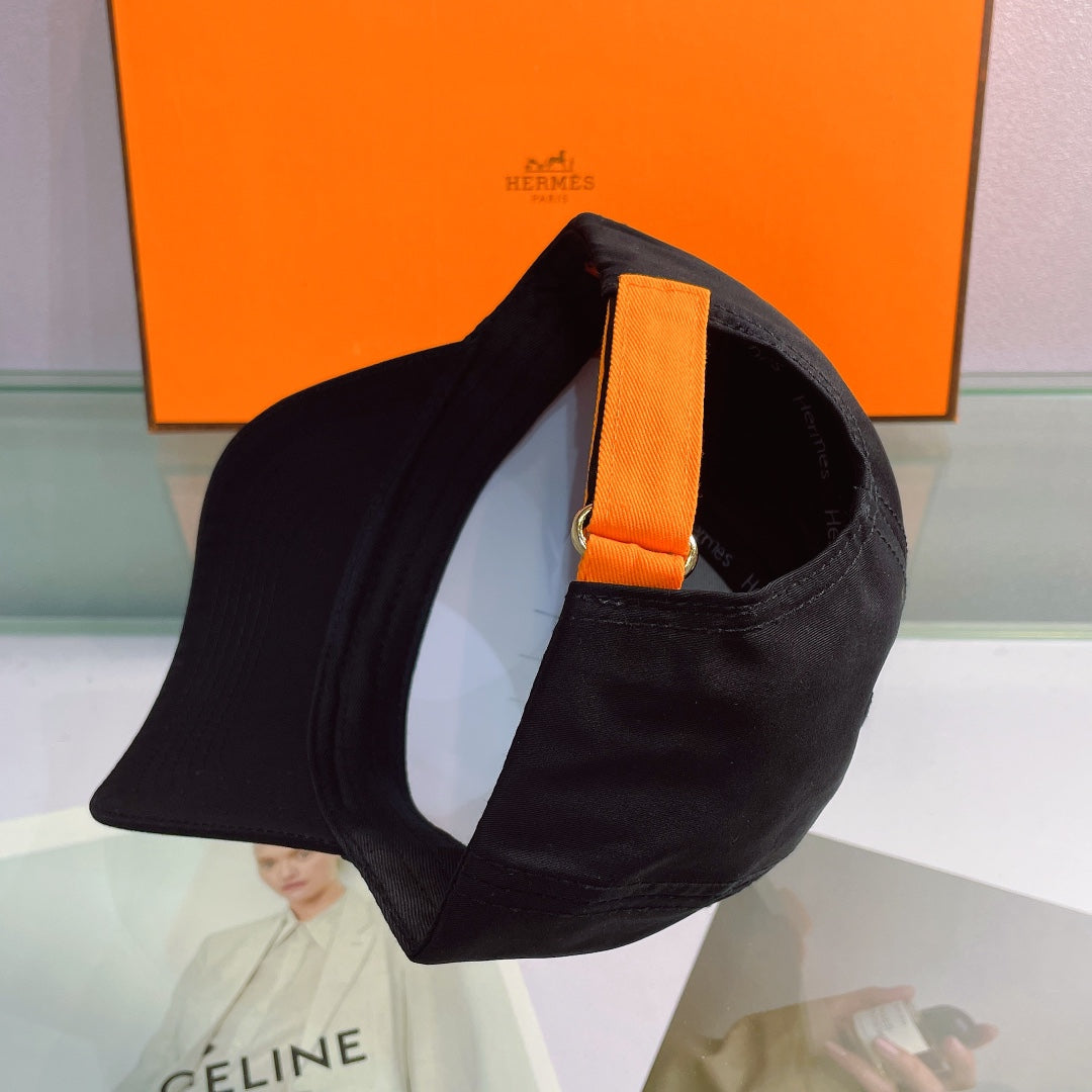 Black cap with orange strap on a reflective surface with an orange Hermes box in the background.