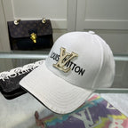 White cap with gold 'Louis Vuitton' logo on a reflective surface with a handbag in the background.