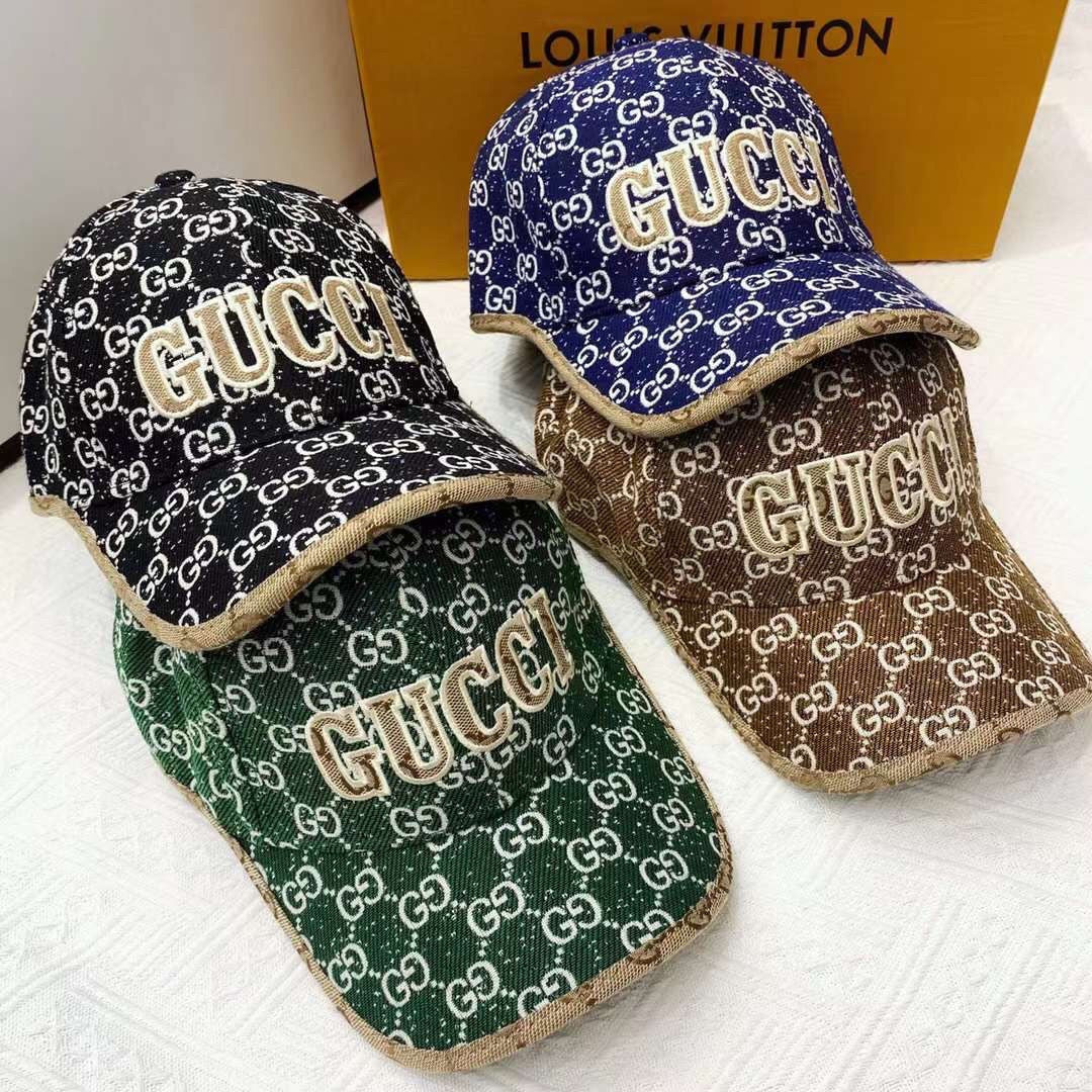 Four Gucci-patterned hats in different colors on a white surface with a Louis Vuitton box in the background.