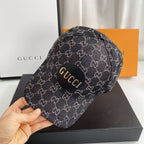 Gucci cap with logo pattern held by a hand, with Gucci box in the background.