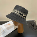 Black straw hat with 'Christian Dior' logo on a mannequin head against a neutral background.
