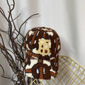 Brown and white patterned blanket on a gold wire basket with branches and a white curtain background