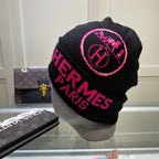 Black beanie with pink 'Hermes Paris' logo on a mannequin head, with a Louis Vuitton handbag in the background.