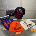 Four Hermes Paris beanies in different colors with visible brand logos on a reflective surface.