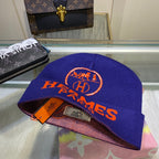 Blue Hermes cap with orange logo on a glass surface