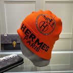 Orange beanie with 'Hermes Paris' logo on a mannequin head, with a Louis Vuitton bag in the background.
