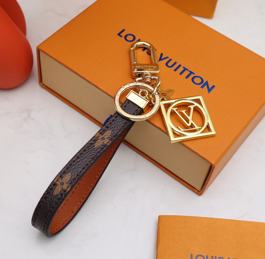 Louis Vuitton monogram leather strap keychain with gold-tone hardware and square charm on orange box